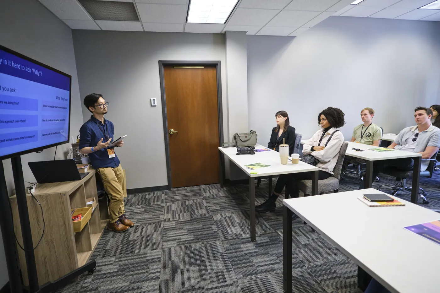 Alan Gi leading a UX design workshop session at AIGA Minnesota Design Camp, presenting a slide on why it is hard to ask "why"